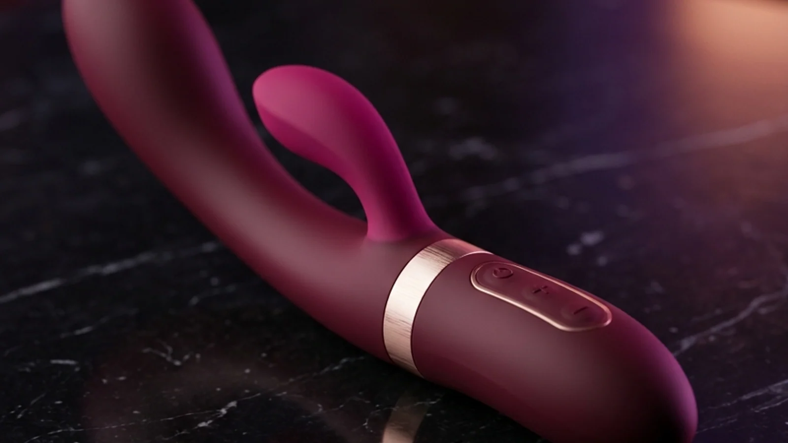 Vibrador ergonómico de silicona médica ciruela con aro de oro rosa sobre mármol italiano